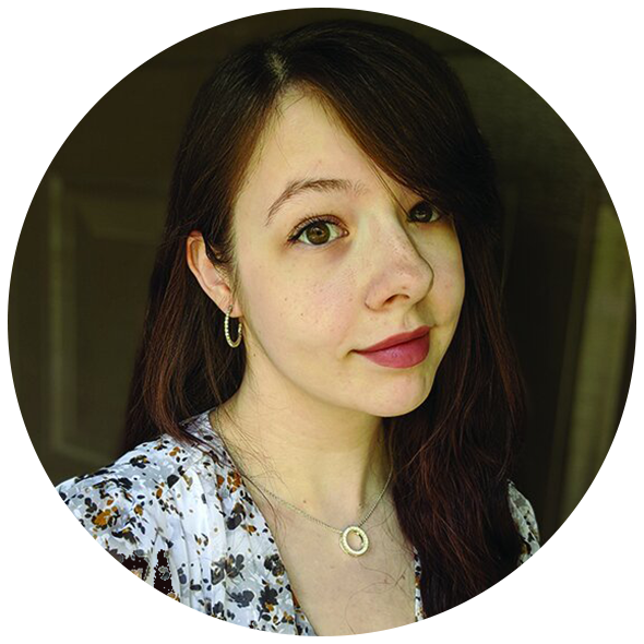 A young woman with dark brown hair wearing a white floral top and jewelry, looking at the camera with a slight smile.